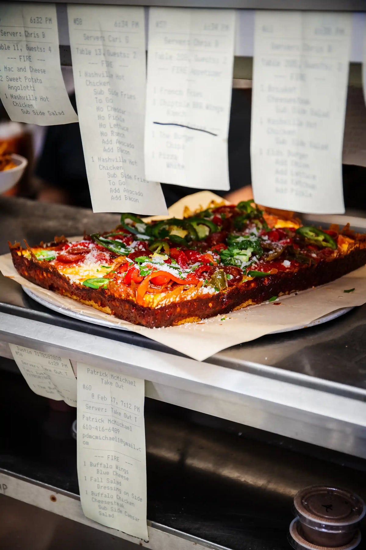 Square pizza with various toppings on a metal surface with paper menus in the background