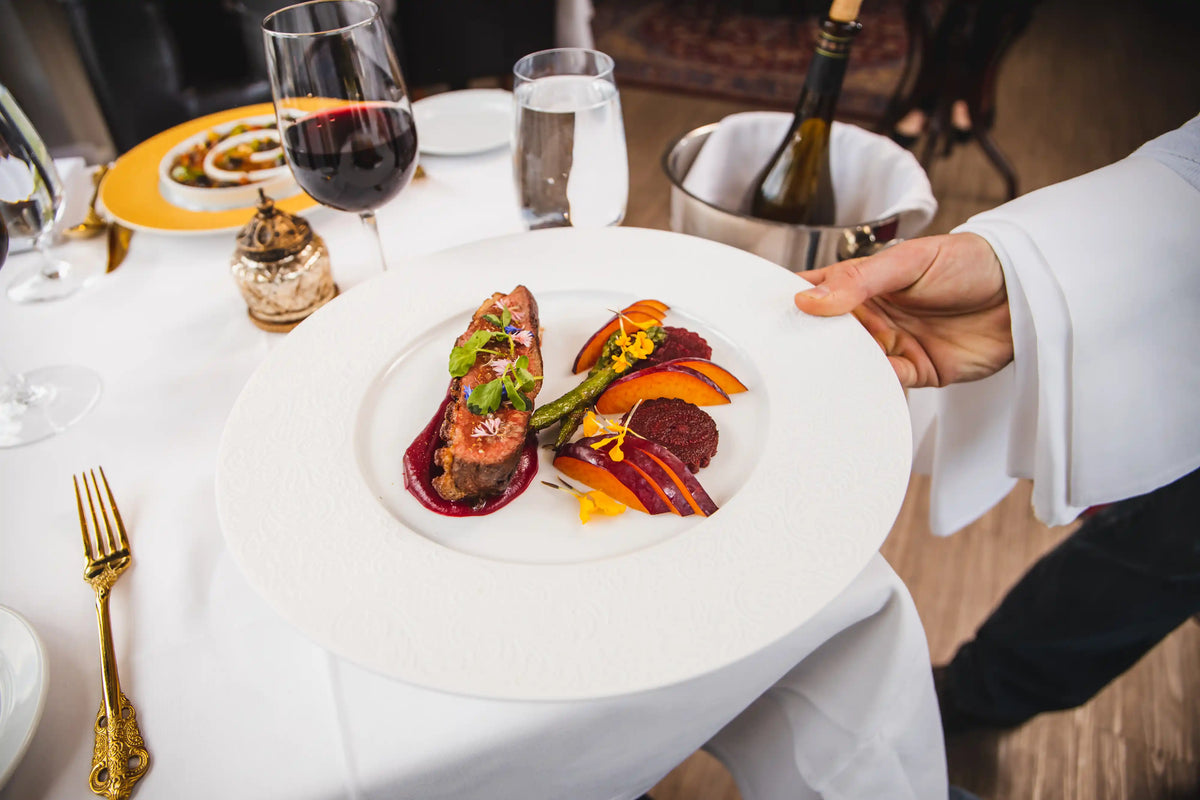 Delicate dish of food on a white plate with a glass of red wine, set on a table.