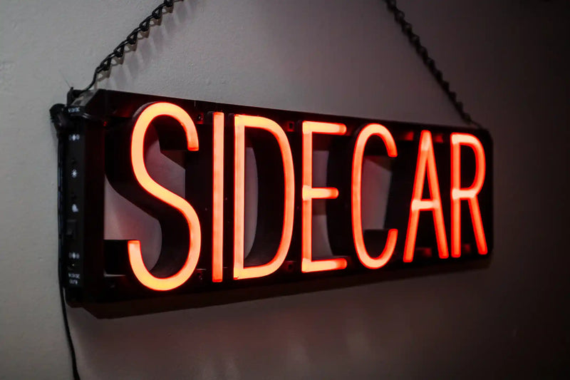 Neon sign with the word 'SIDECAR' on a dark background