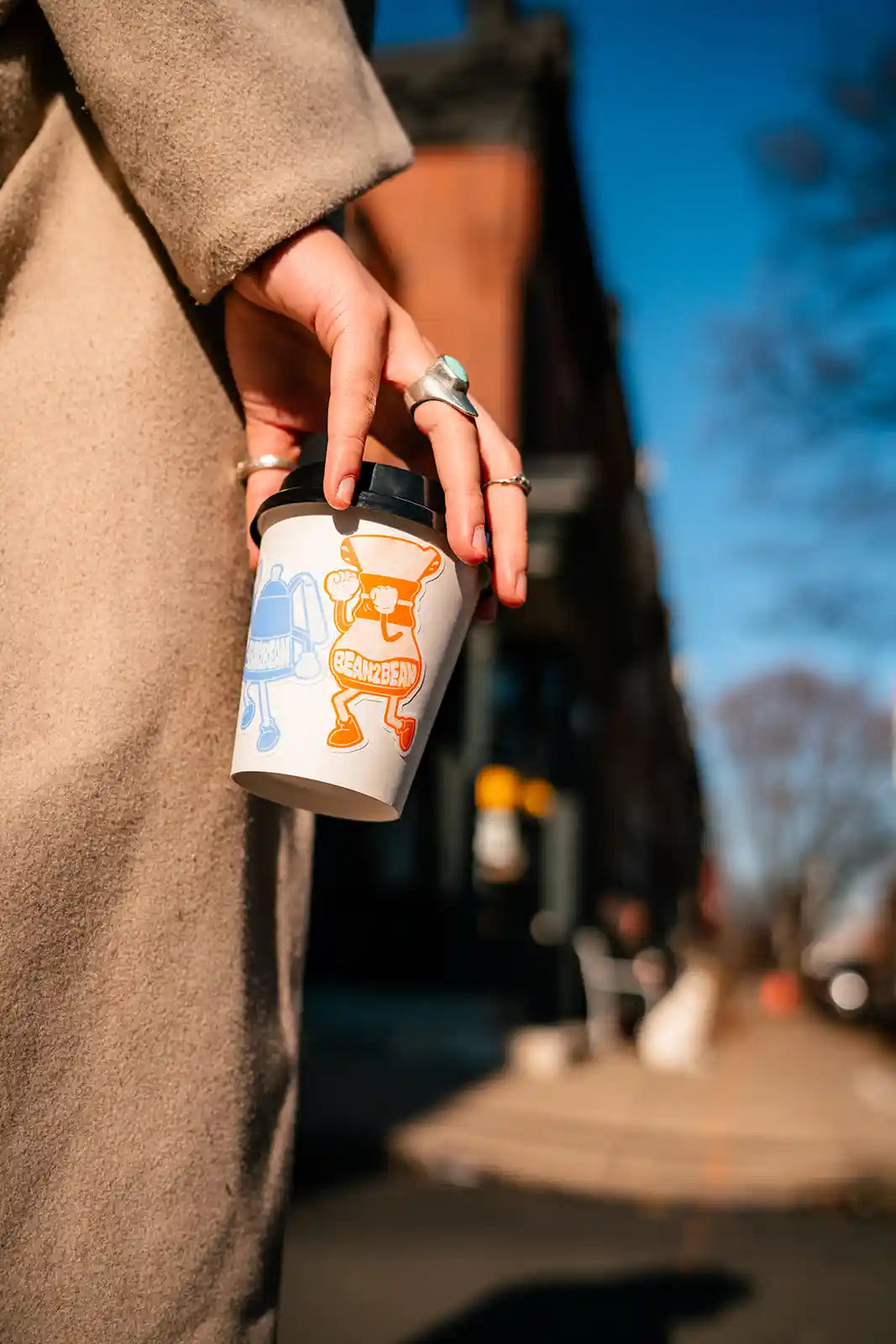 Person holding a coffee cup with a cartoon character design outdoors on a sunny day.