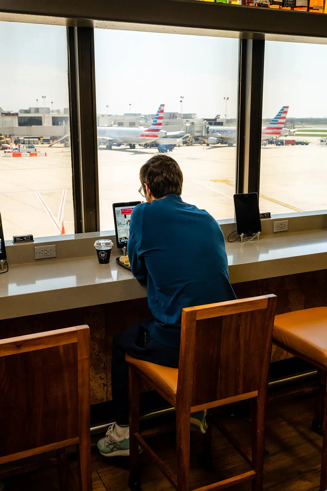 Person sitting at a counter in the PHL airport using a laptop with airplanes visible outside the window.