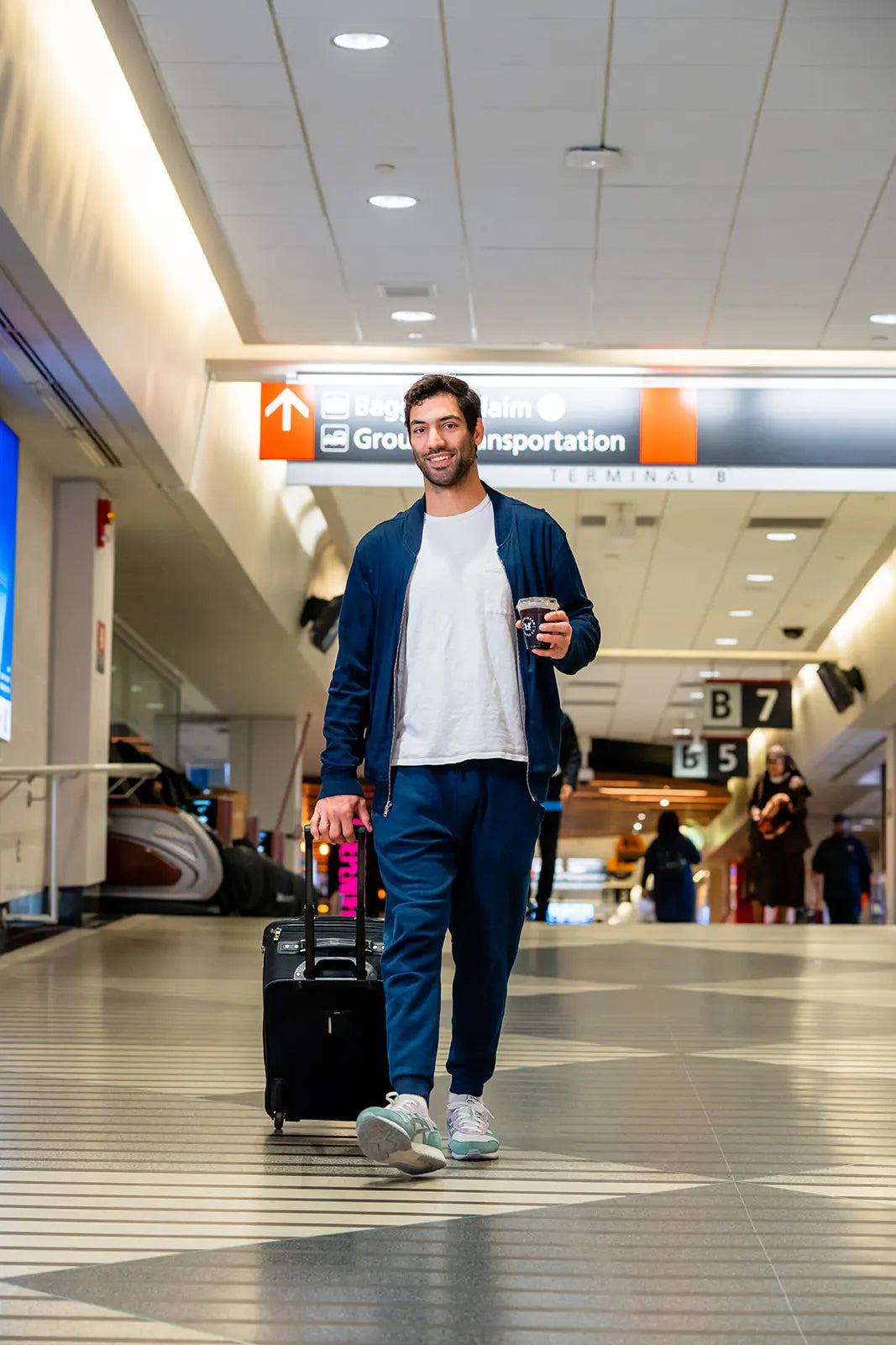 man walking with luggage holding a Bean2Bean Coffee cold brew at Philadelphia International Airport