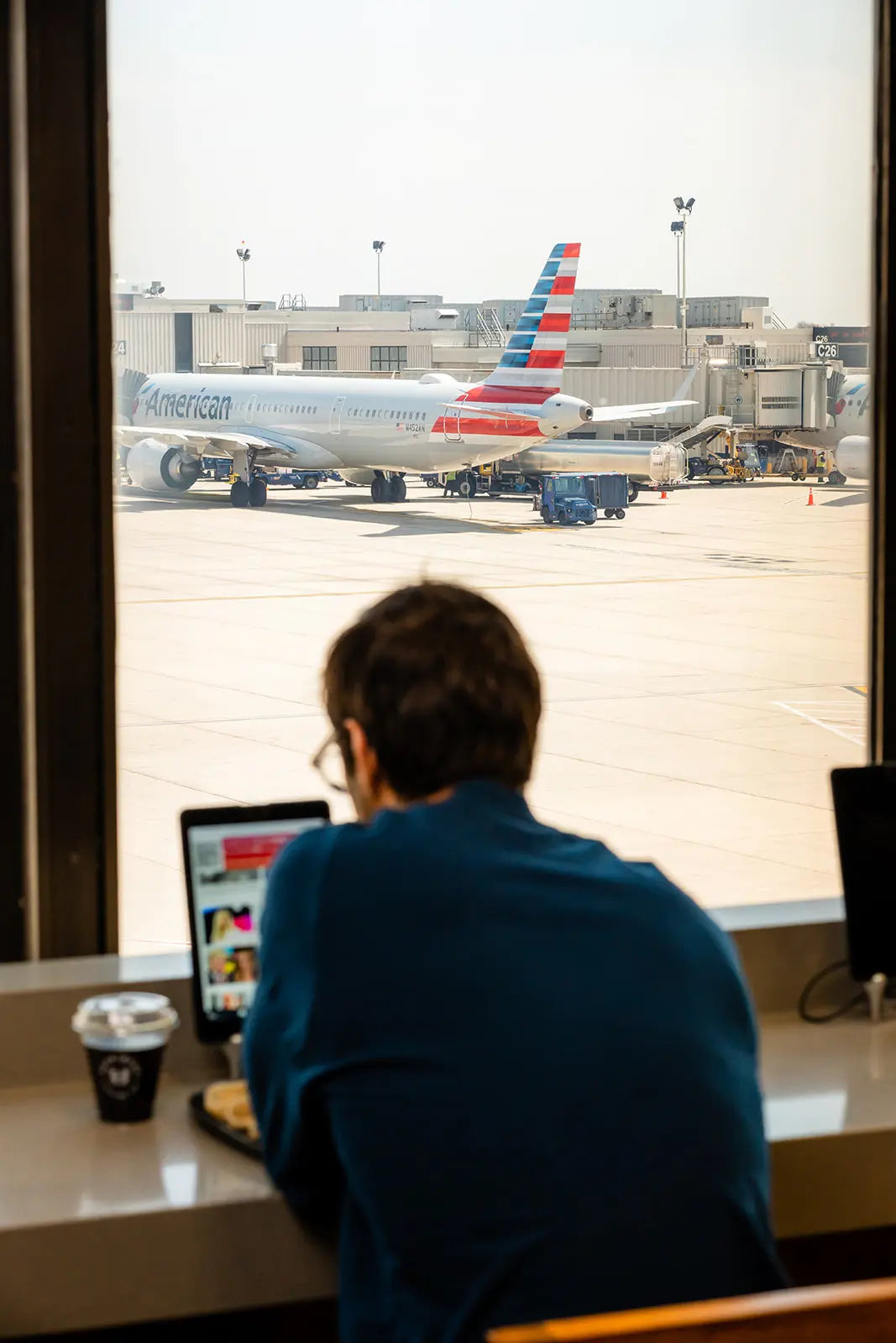 Person using a laptop at PHL airport with an American Airlines plane visible through the window.