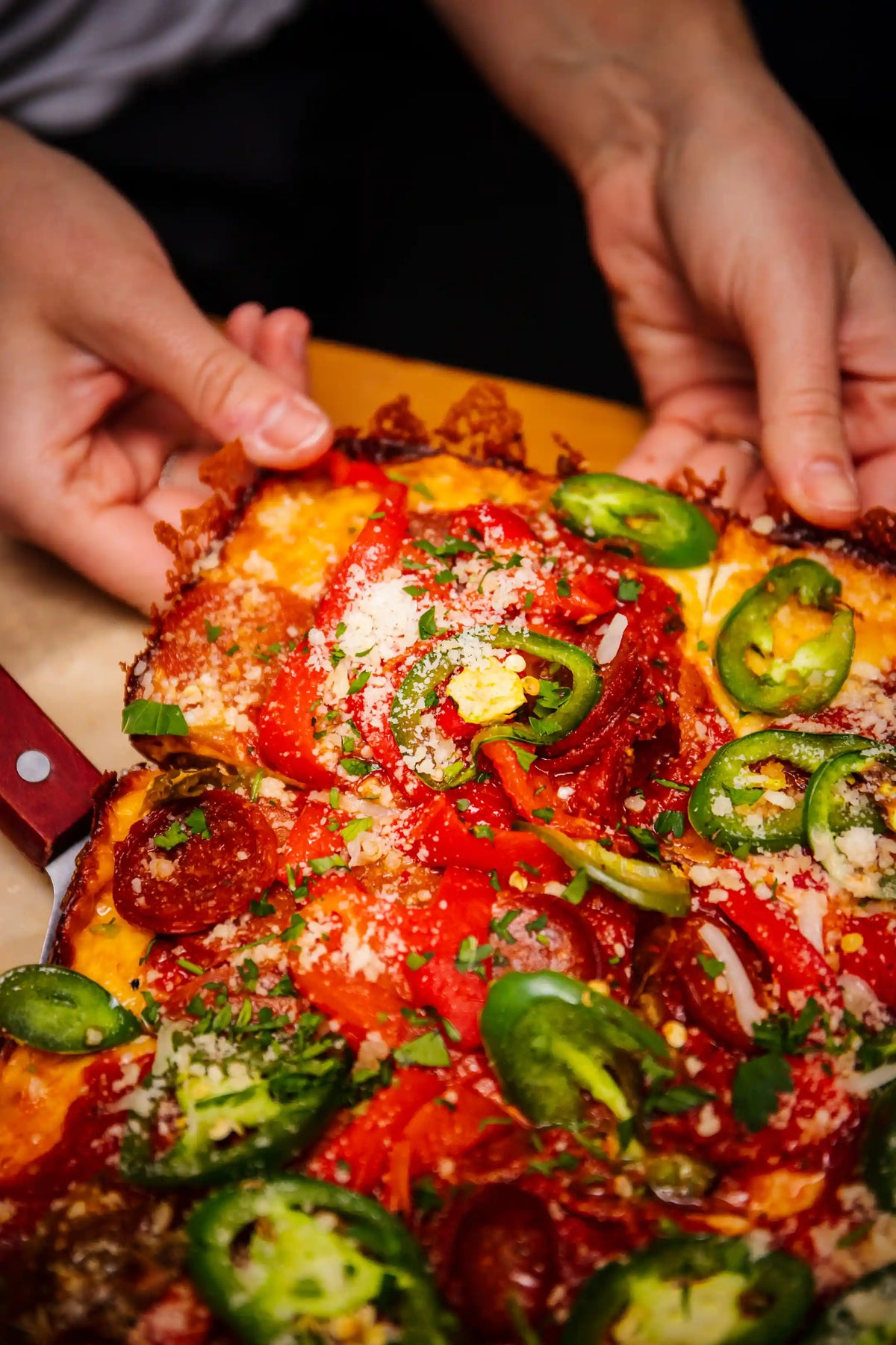 Person holding a pizza with jalapeños, pepperoni, and cheese