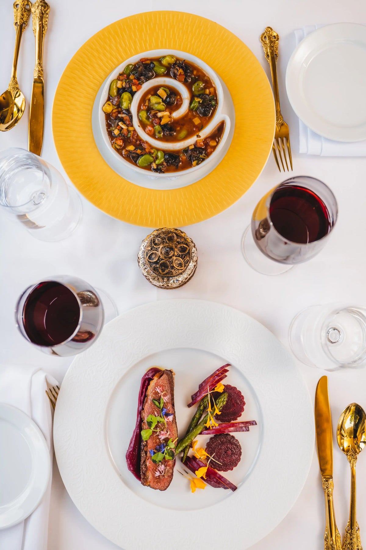 Elegant dinner table setting with gourmet dishes, red wine, and gold cutlery.
