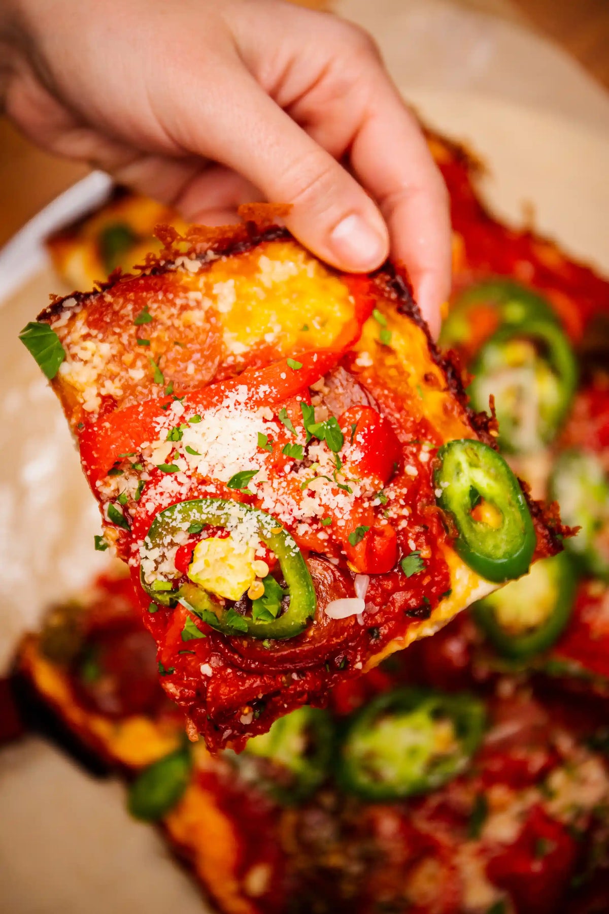 Hand holding a slice of pizza with jalapeños and cheese