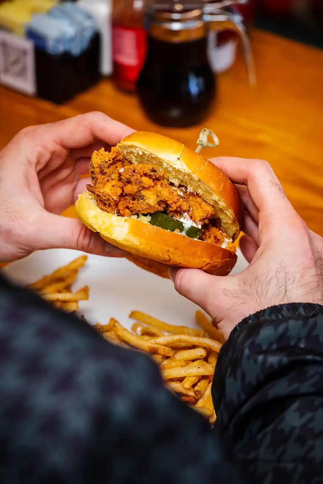 Person holding fried chicken sandwich with fries on a wooden table