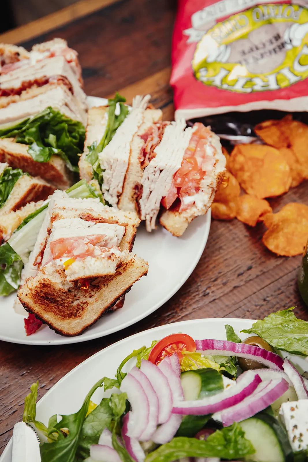 Plated sandwiches and salad on a wooden table with a packet of salt in the background.