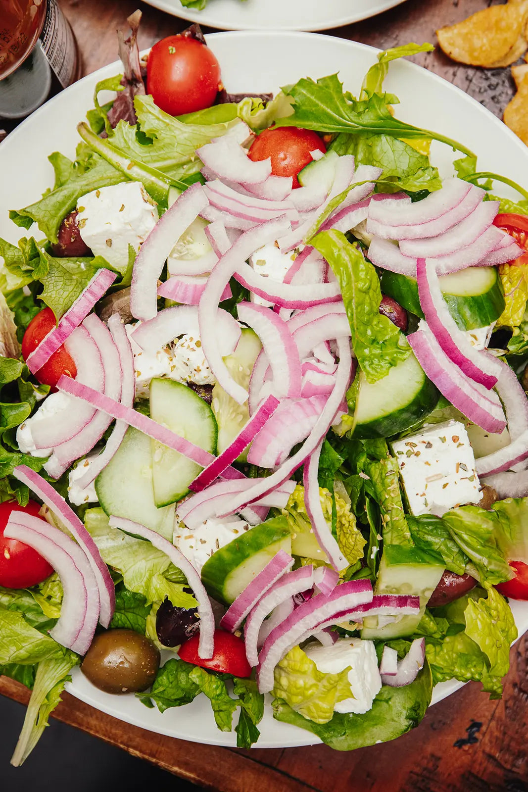 Greek salad with cucumbers, tomatoes, onions, feta cheese, and olives on a white plate.