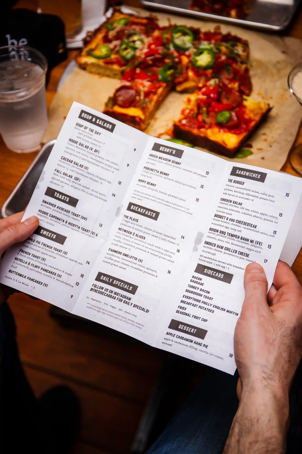 Person holding a restaurant menu with a pizza in the background