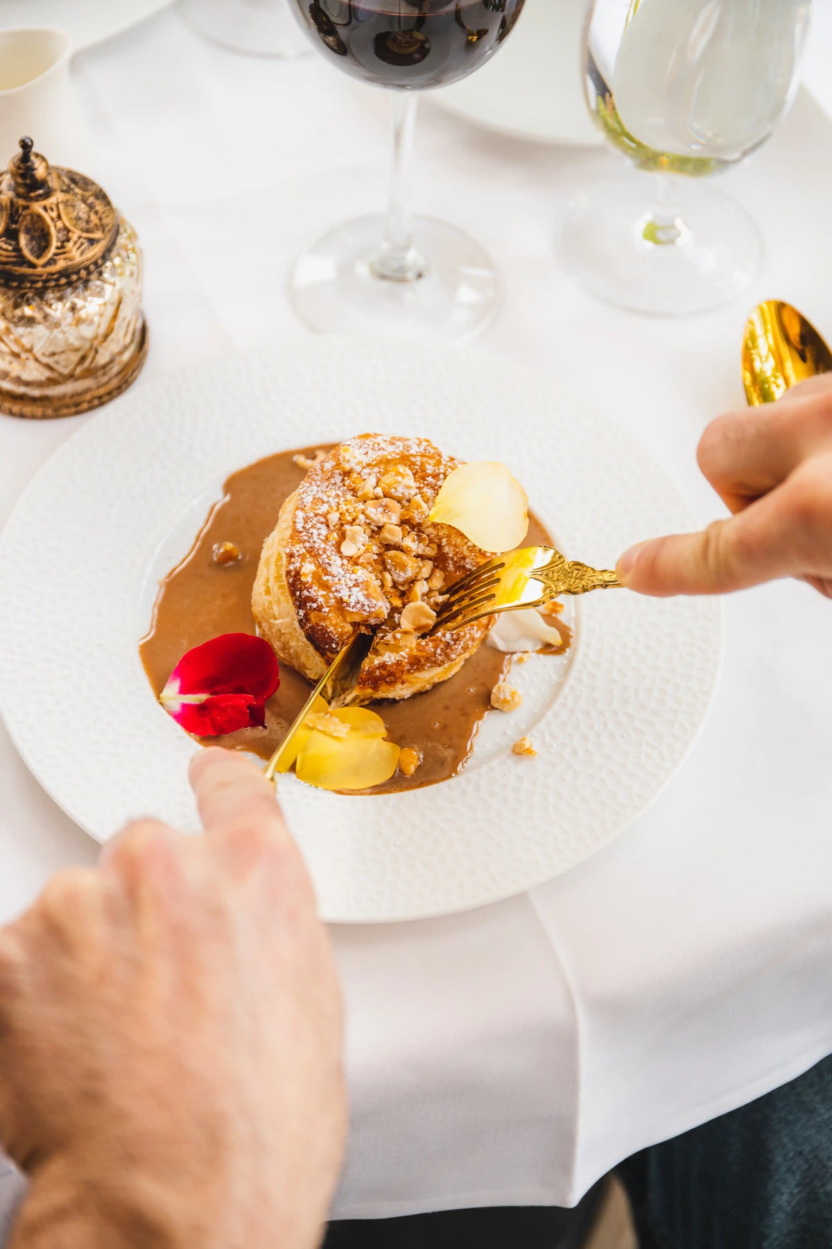 Person eating dessert with a fork on a white plate, surrounded by wine glasses.