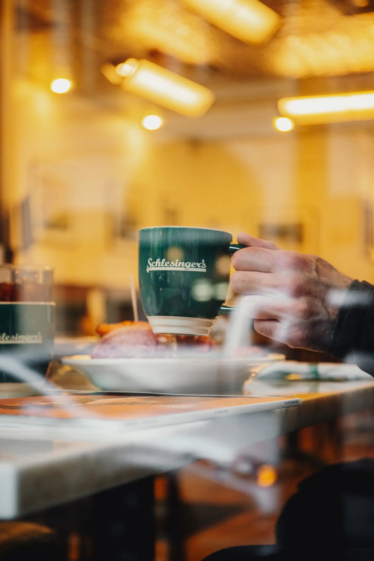 Person holding a Schlesingers coffee mug in a cozy indoor setting