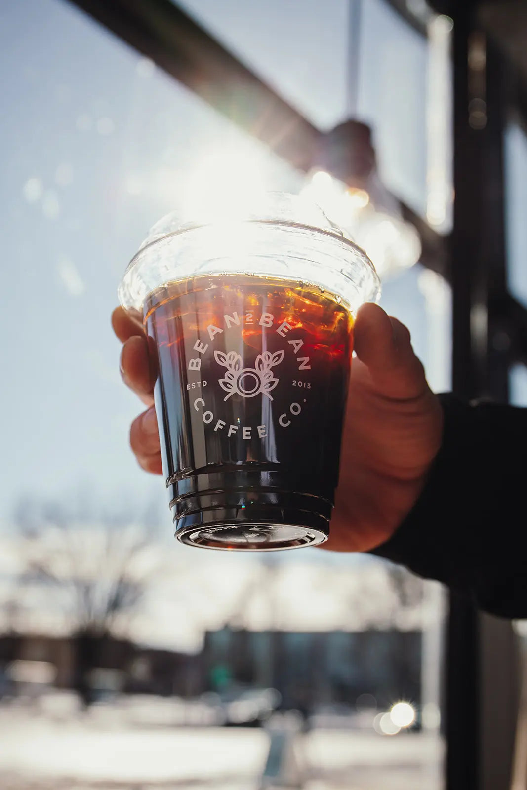 Hand holding a cup of coffee from Bean2Bean Coffee Co. with a blurred outdoor background.