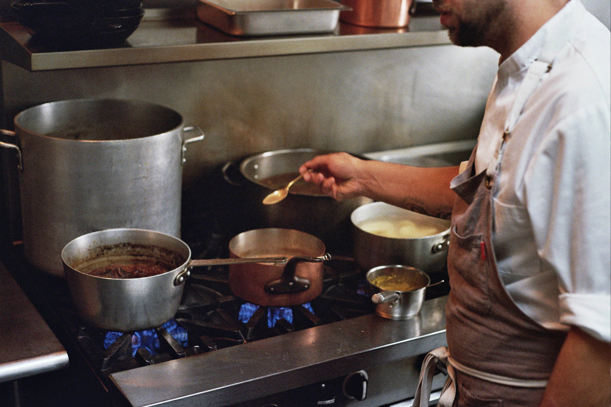 Person cooking in a kitchen with pots and pans on a stove