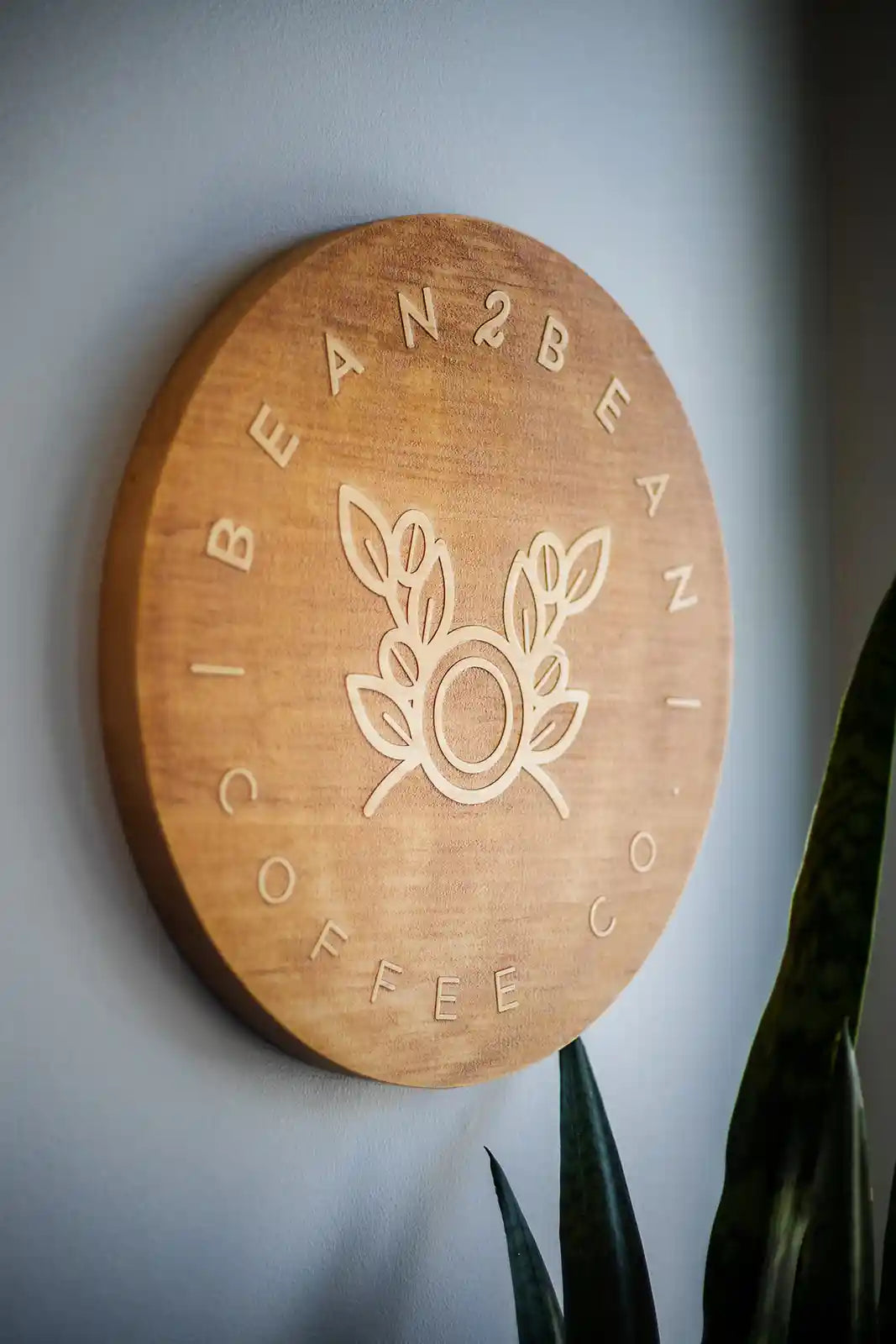 Wooden sign with 'Bean2Bean Coffee Co.' logo on a gray wall.