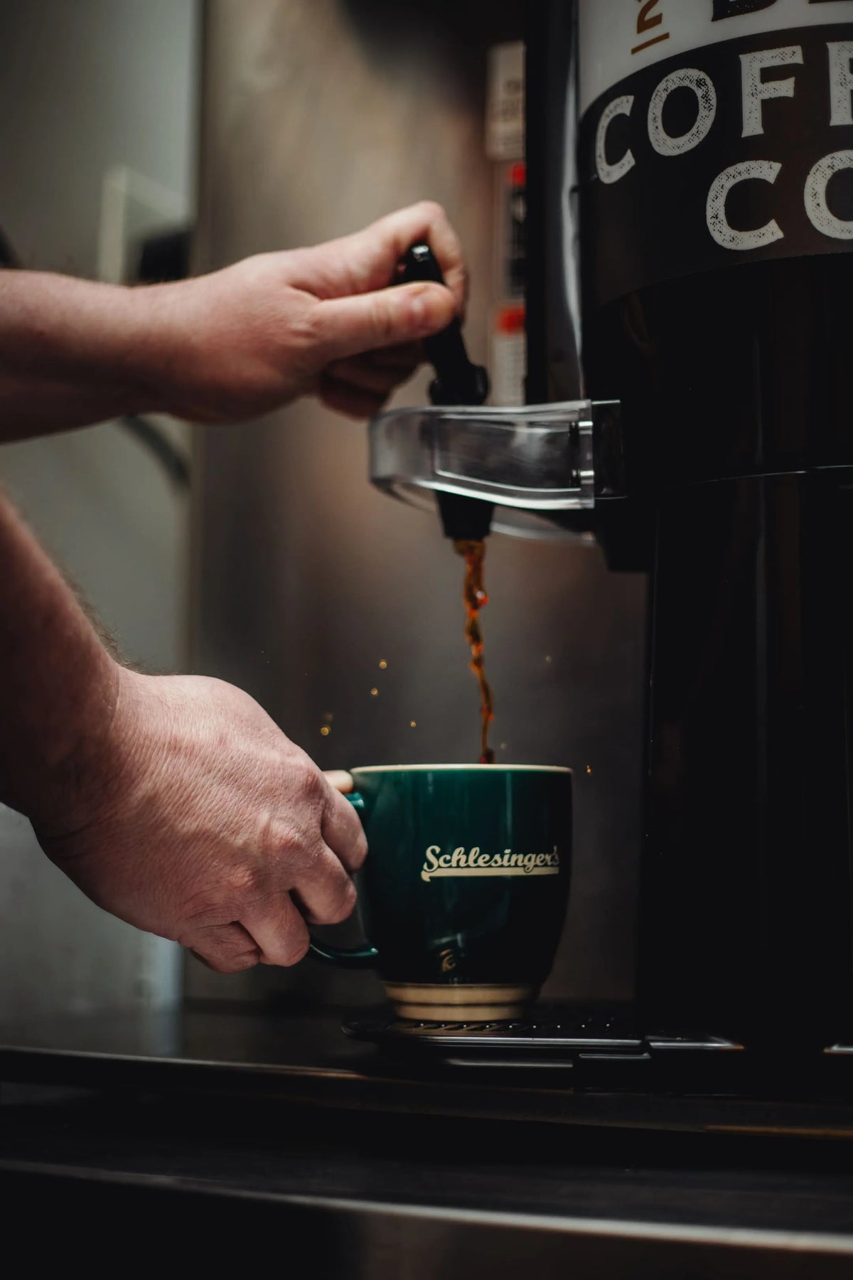 Person pouring coffee from a pot into a green mug.