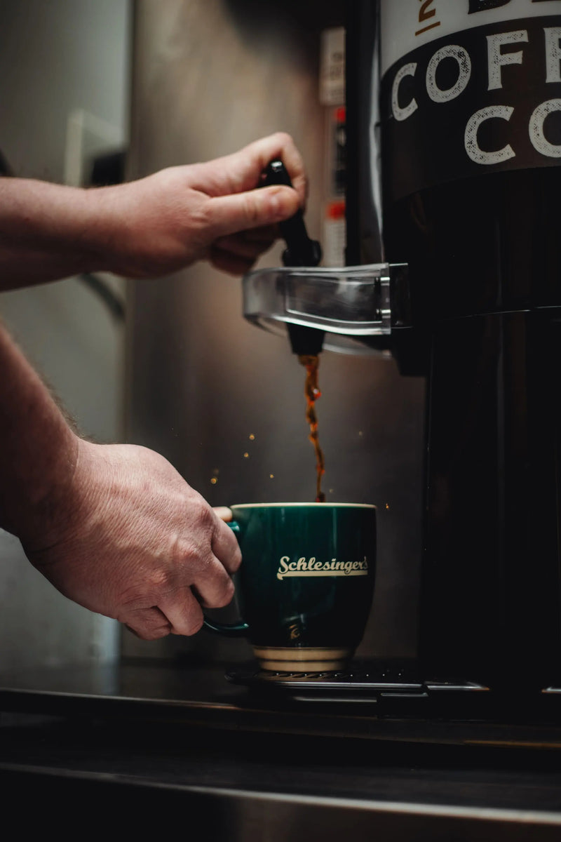 Person pouring coffee from a pot into a green mug.