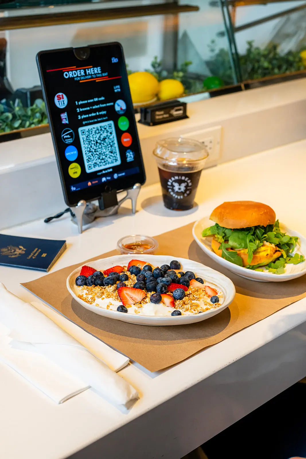 Table with a touch tablet displaying a QR code, two plates of food, and a Bean2Bean Cold Brew