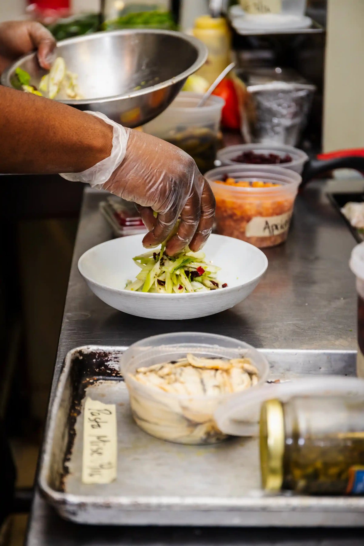 Person preparing a salad in a kitchen setting with various ingredients and utensils.
