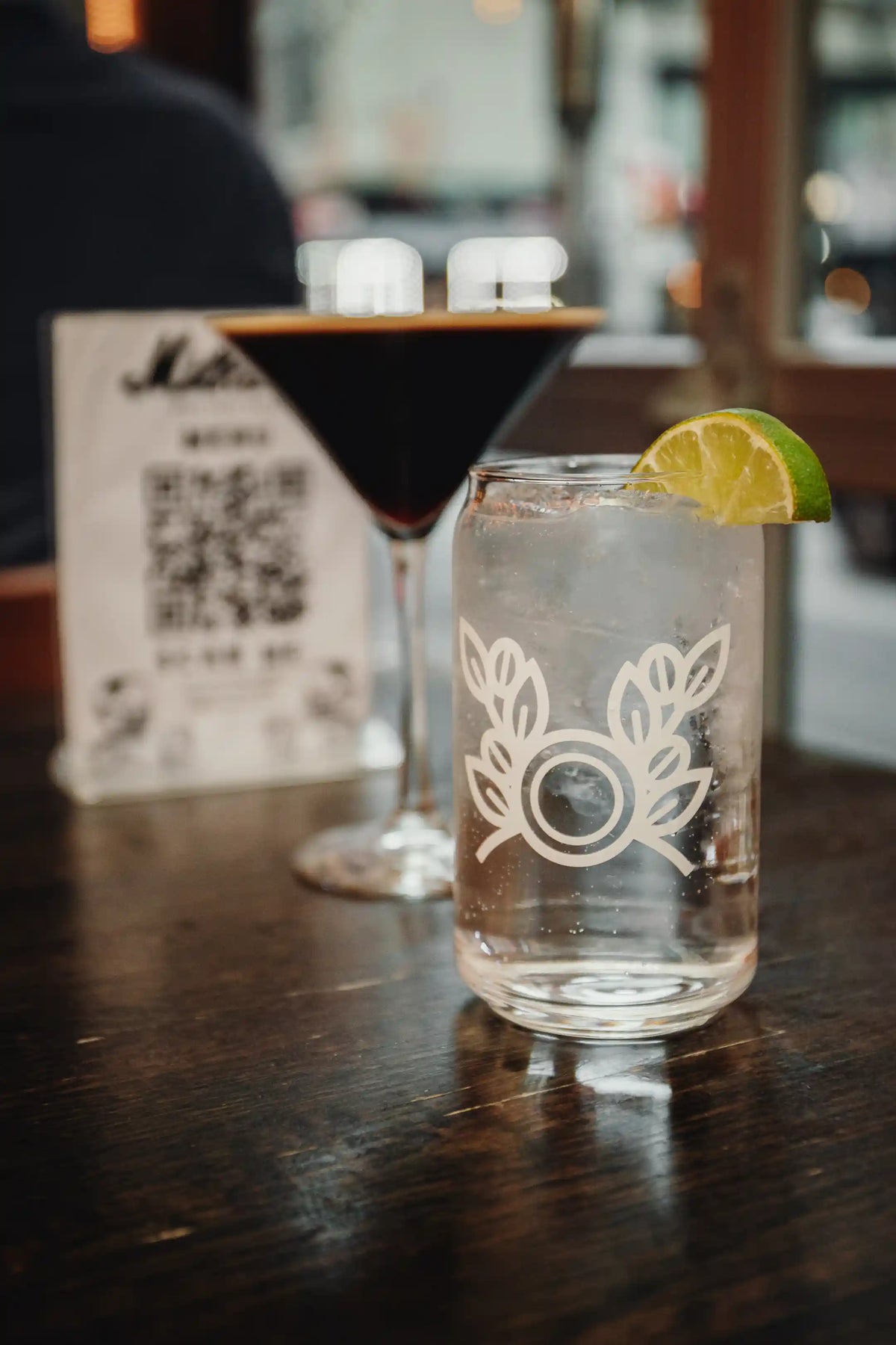 Two cocktails on a bar with a QR code menu in the background