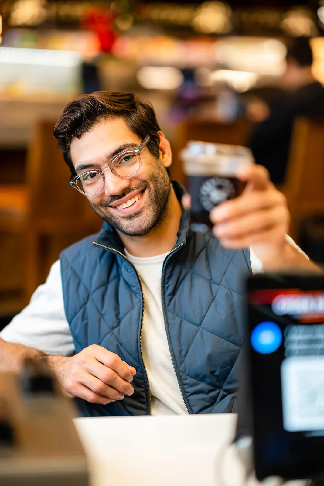 Man holding a Bean2Bean Cold Brew with a blurred background of a cafe.