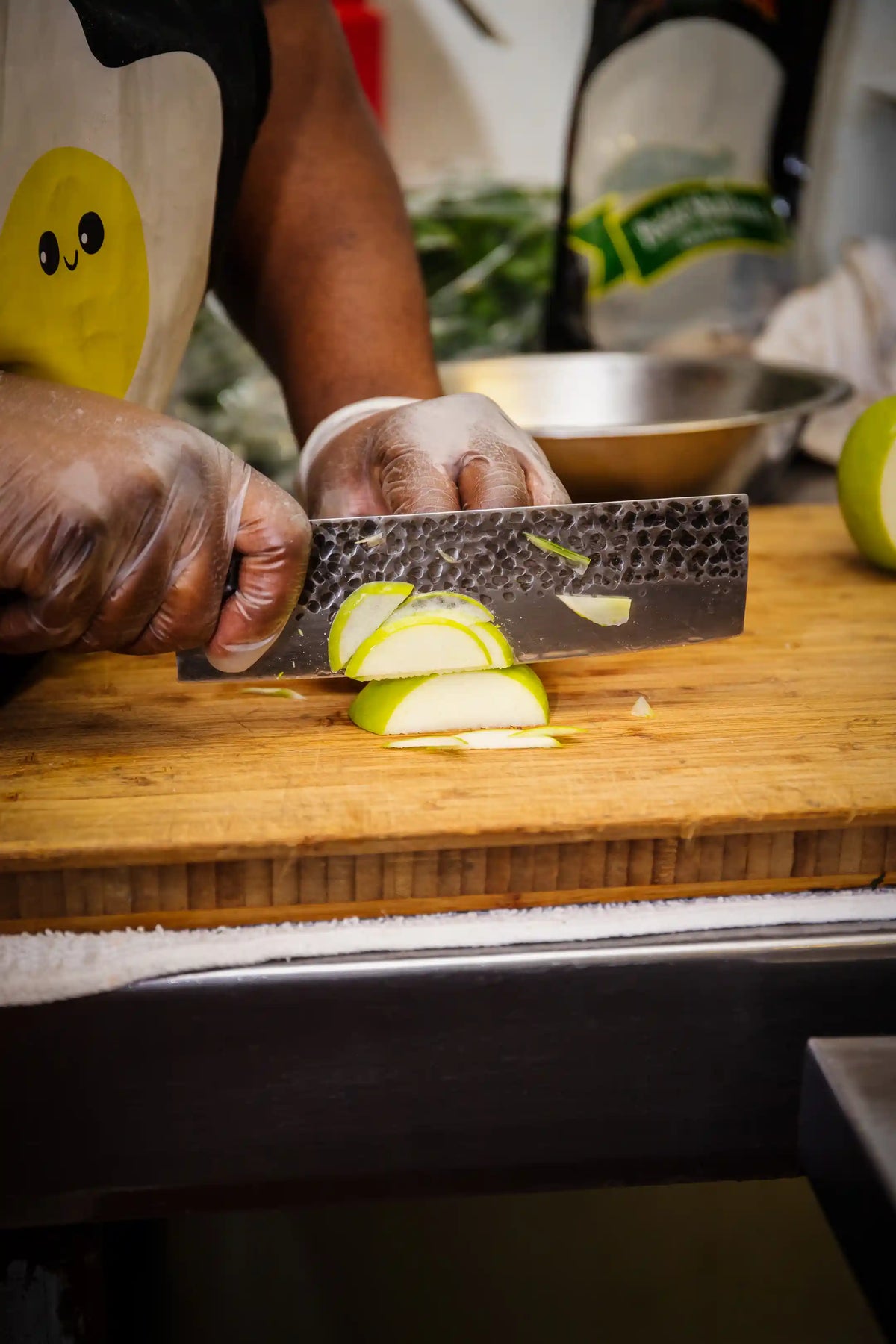 Person slicing green apples on a wooden cutting board with a knife.