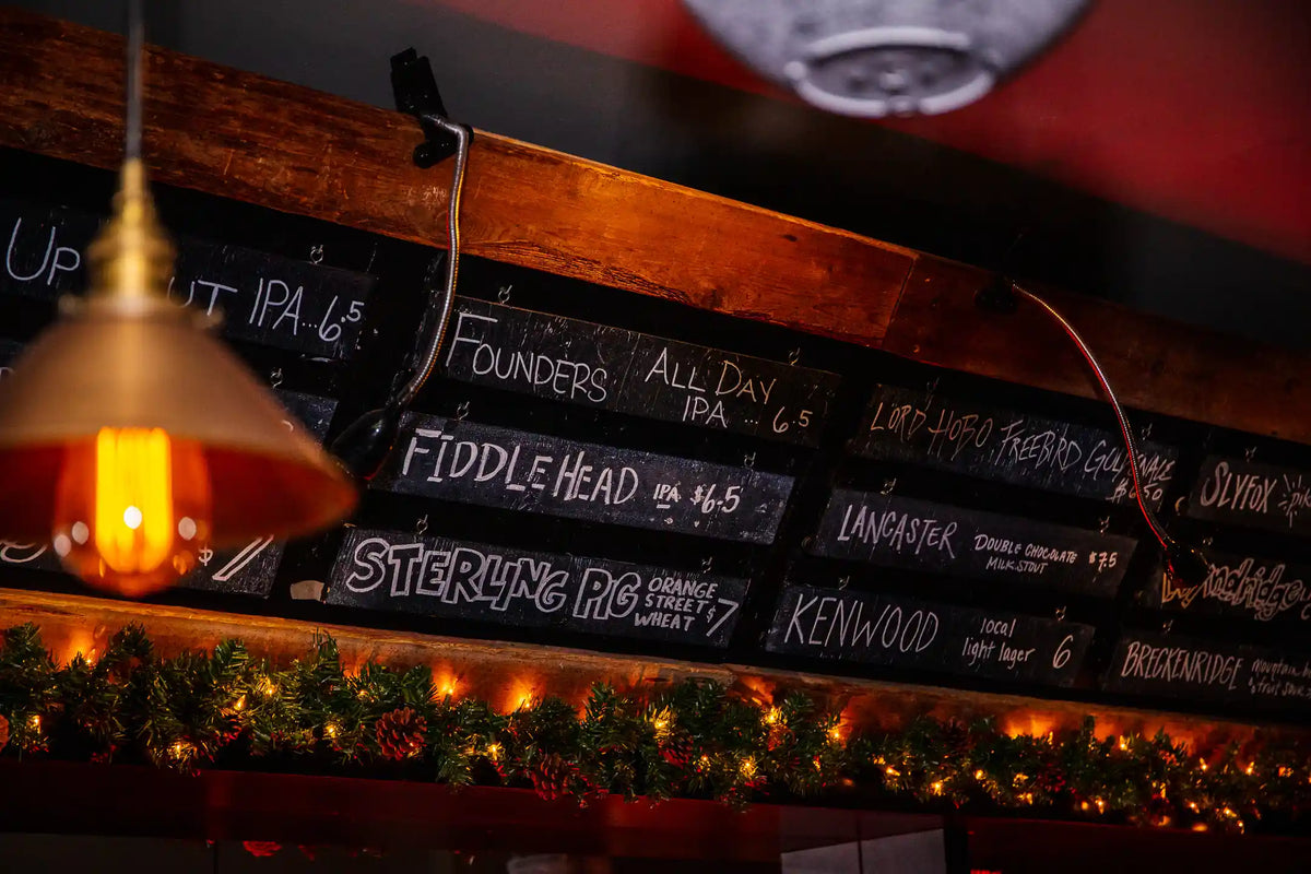 Wooden bar with chalkboard signs displaying beer names and prices, warm lighting.