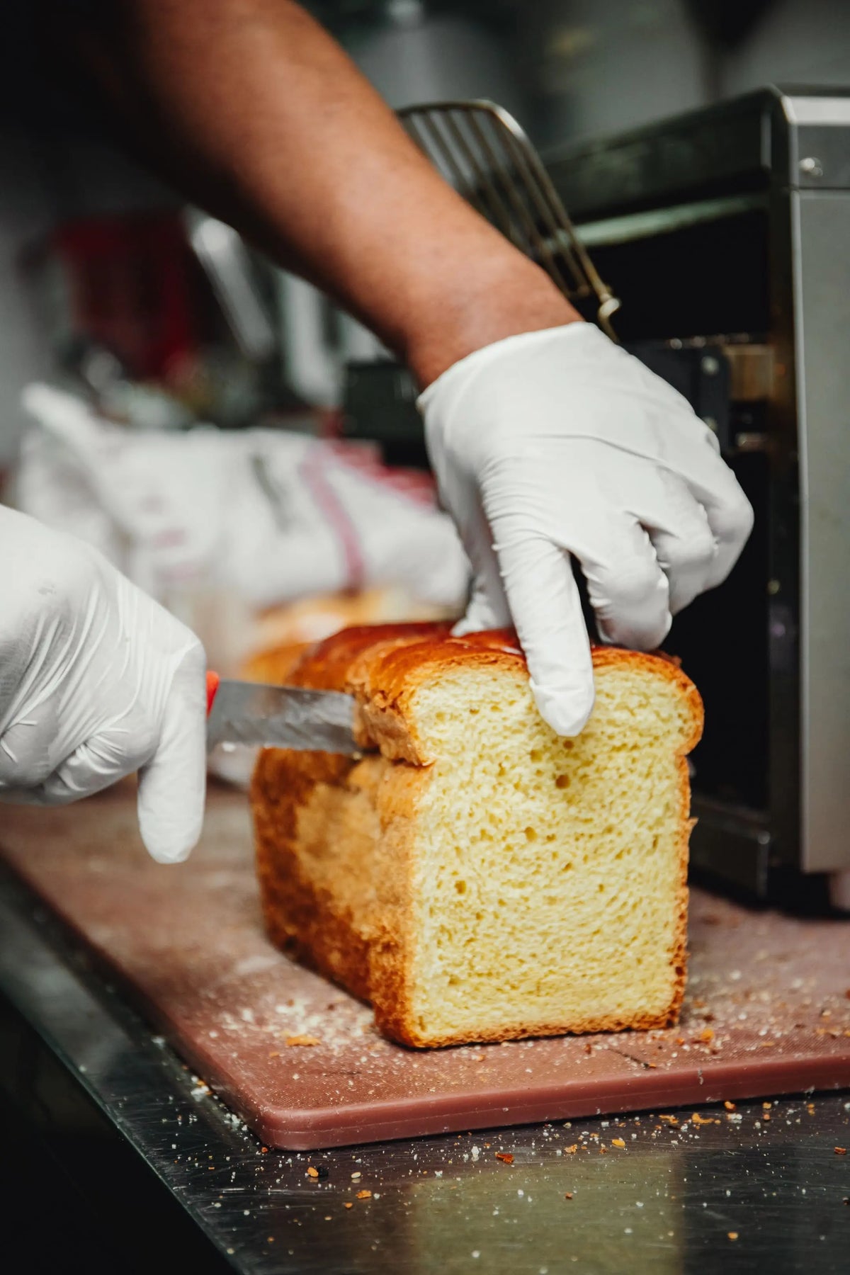 Person cutting a loaf of bread with white gloves in a kitchen setting