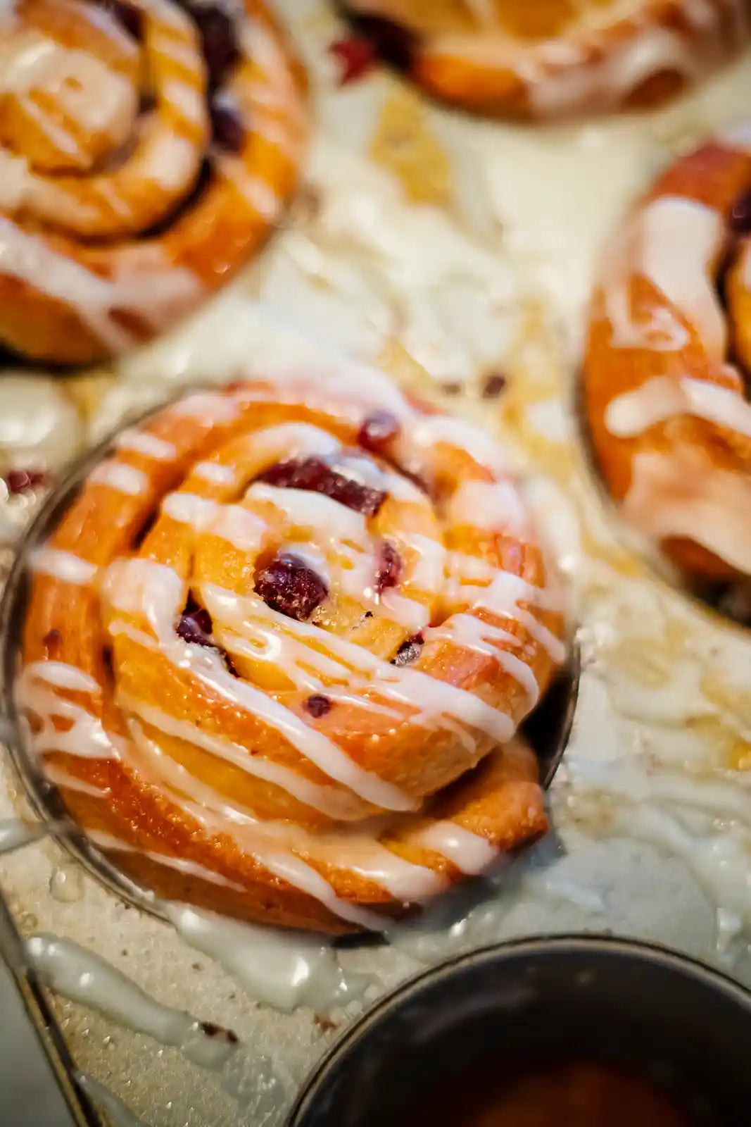 Cinnamon rolls with icing in a muffin tin on a marble surface