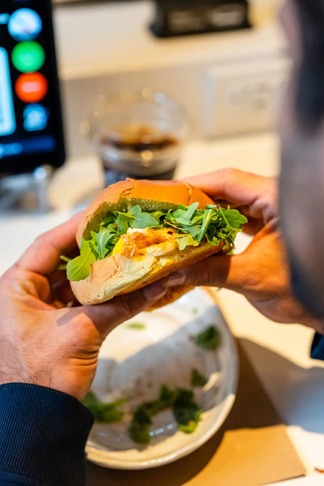 Person holding a sandwich with lettuce at Boule Cafe