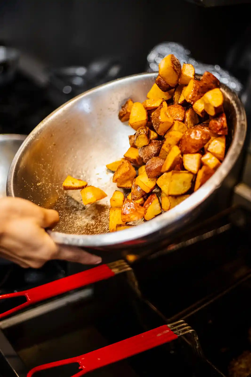 seasoning potatoes in a stainless steel bowl near a stove.