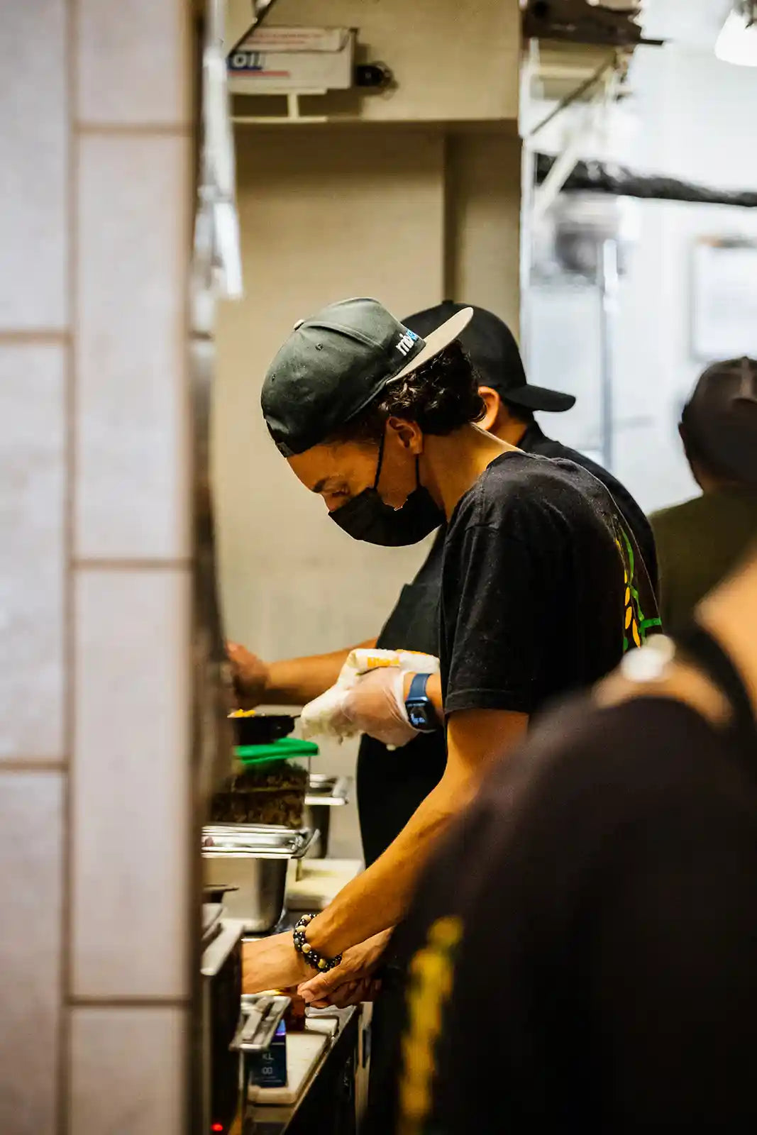 Person working in a kitchen wearing a black t-shirt and cap.