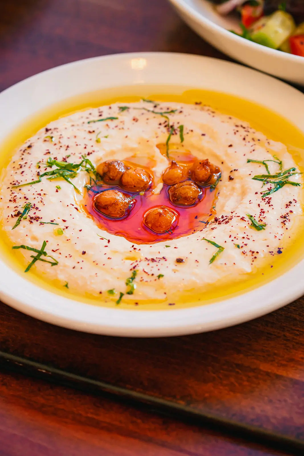 Hummus dish topped with baked chickpeas and herbs on a wooden table