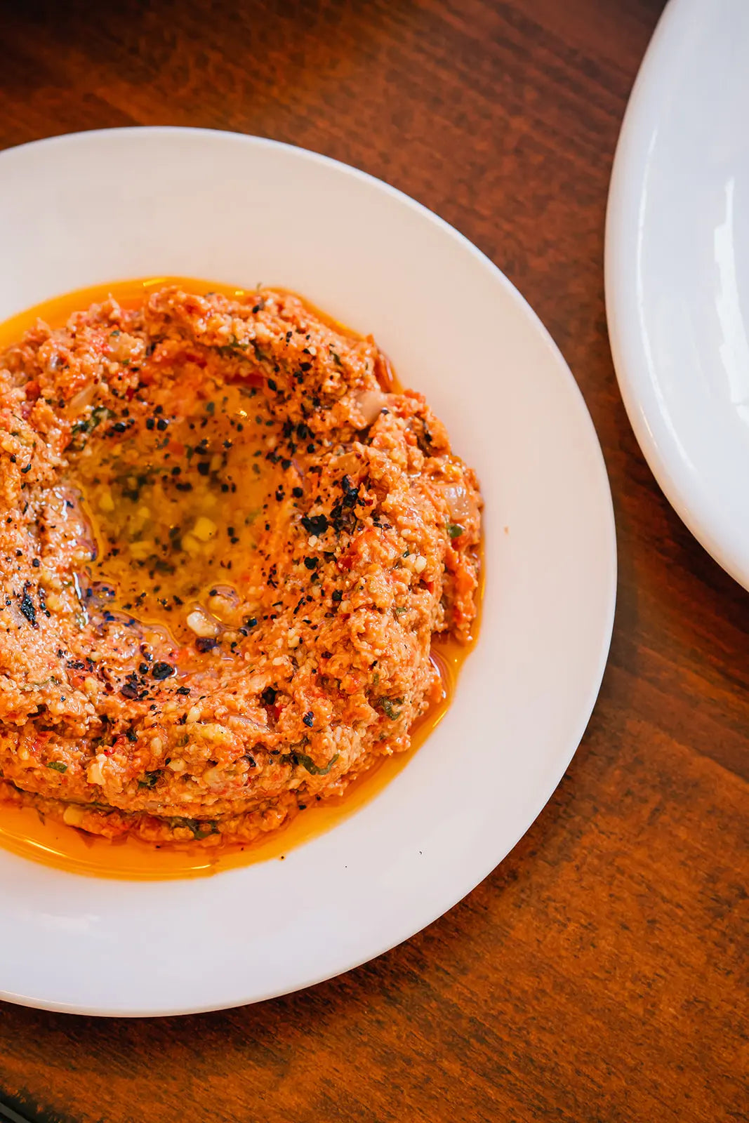 Muhammara in a white dish on a wooden table
