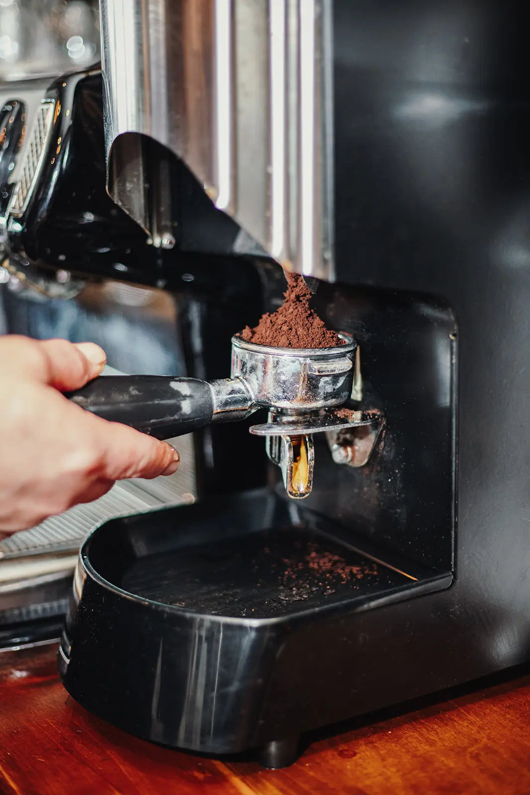 Hand pressing coffee grounds into a portafilter of an espresso machine.