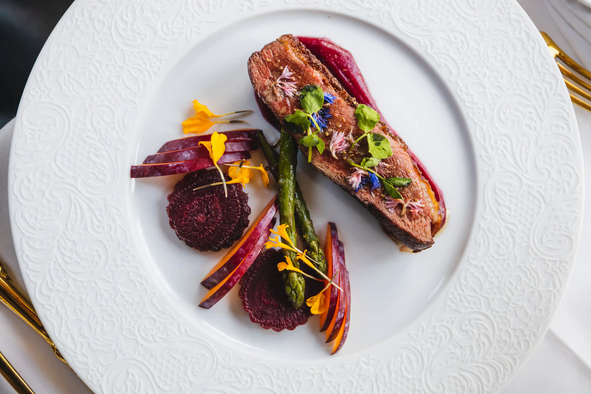 Delicate dish of roasted duck or steak with roasted vegetables on a white plate