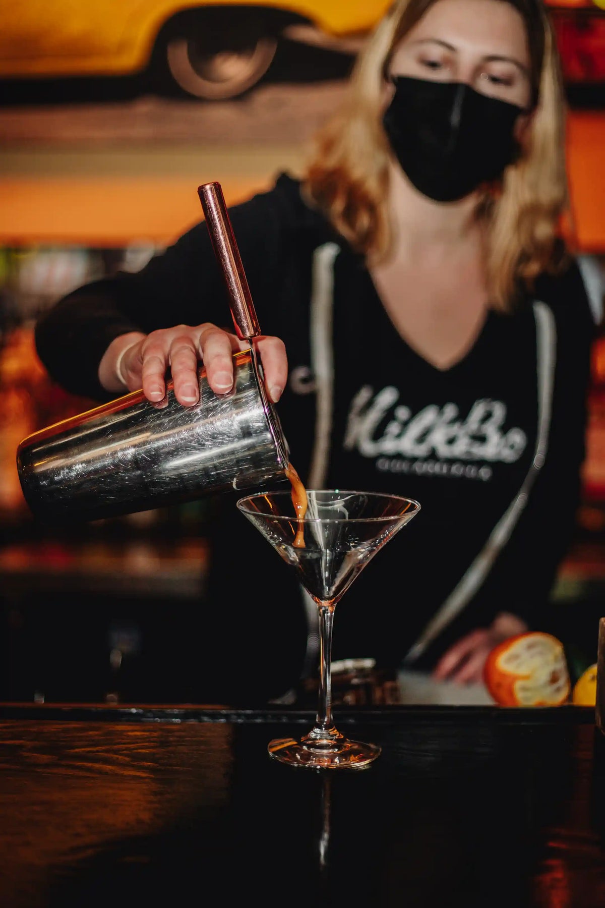 Person pouring espresso martiini into a martini glass with a blurred background
