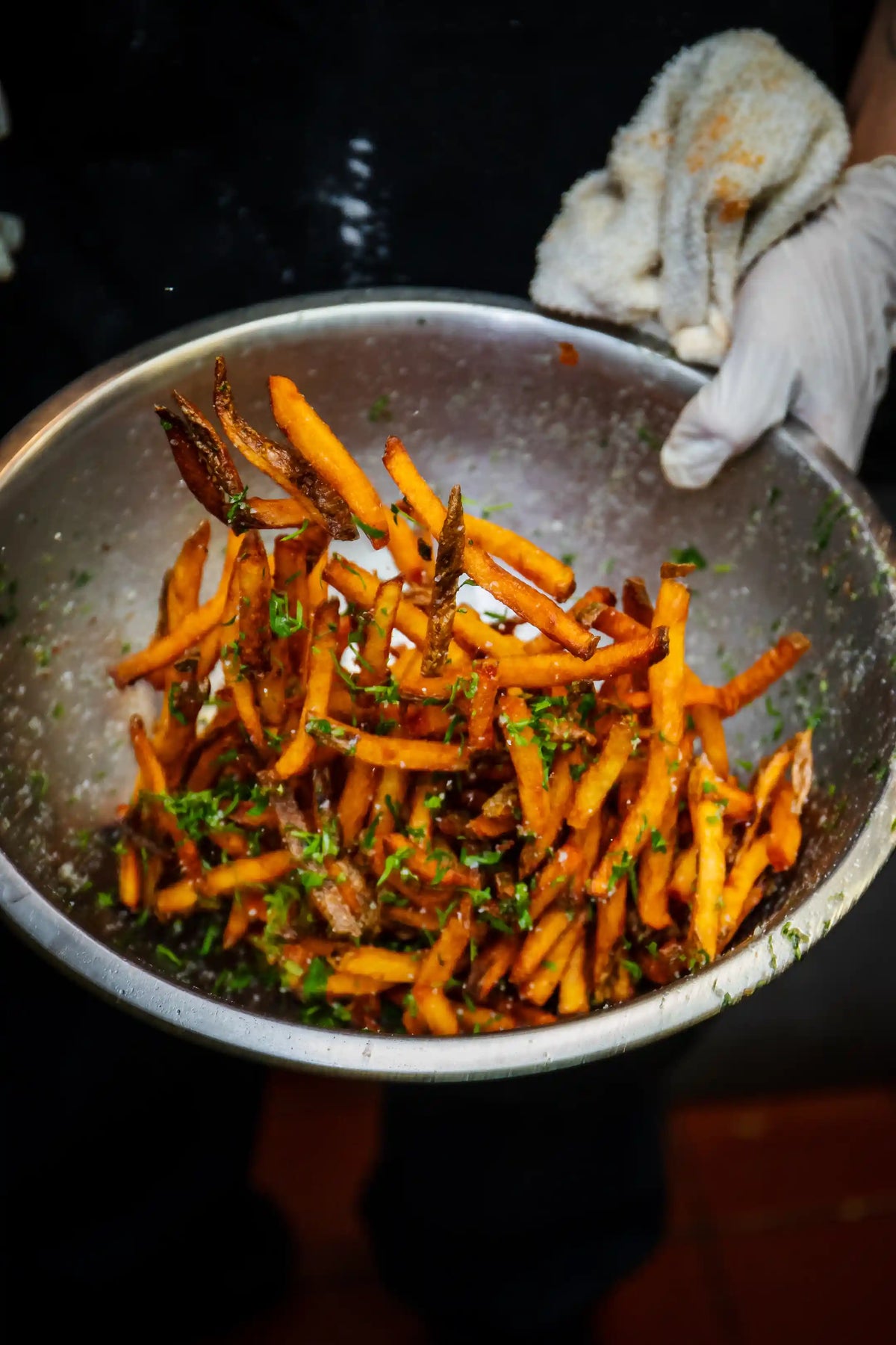fries with herbs in a metal pan held by a gloved hand.