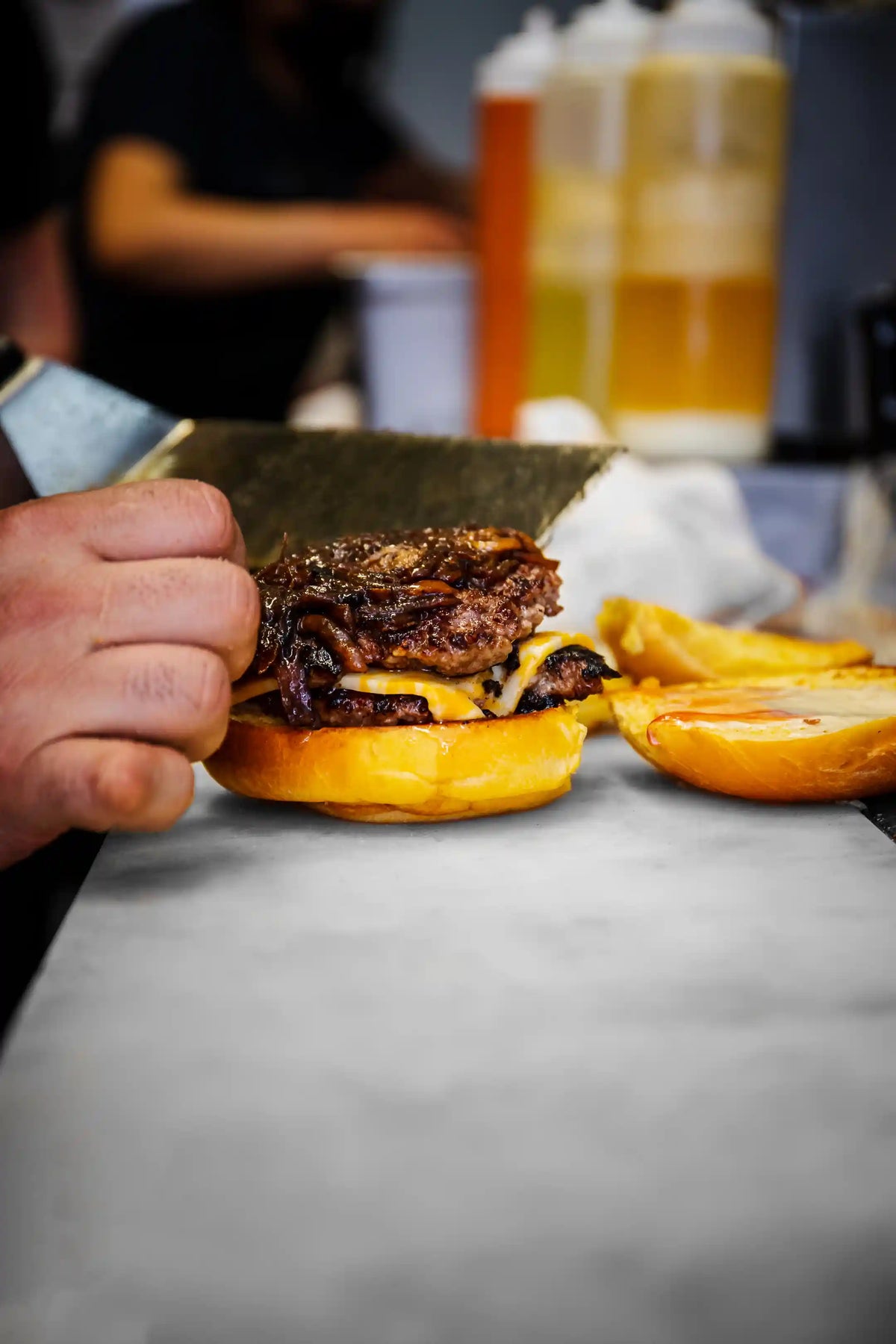 Close-up of a hand placing a burger onto a bun with spatula with a blurred background