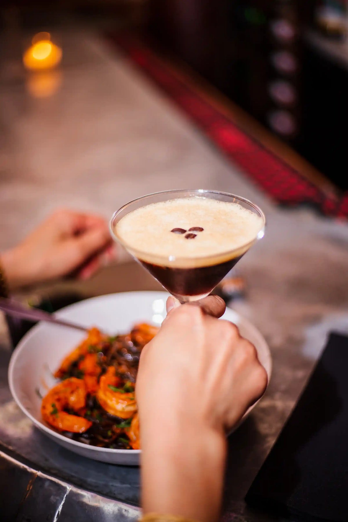 Person holding a martini glass with a dish of food on a table