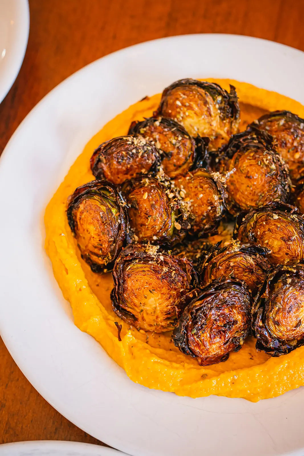 Baked brussels sprouts on a bed of creamy hummus on a white plate.