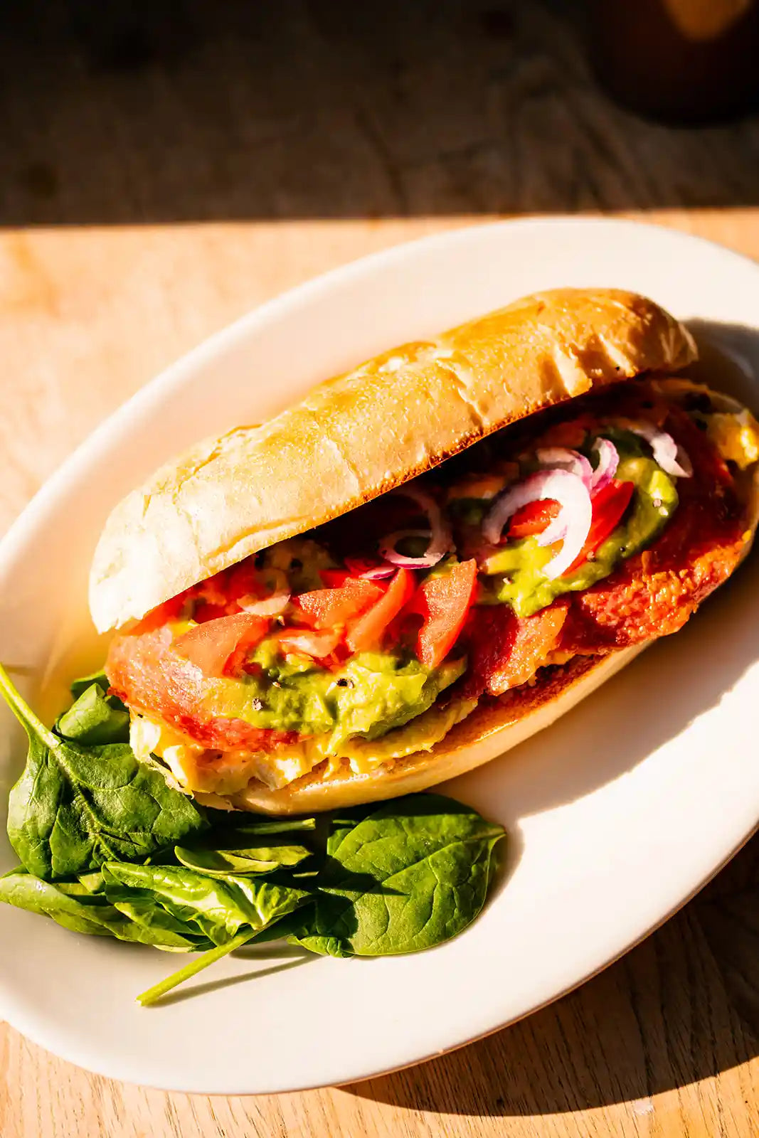 Colorful sandwich on a long roll with vegetables on a white plate