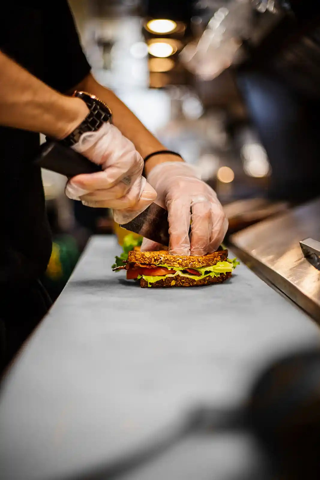 Person assembling a sandwich with bacon, lettuce, and tomato on a kitchen counter.
