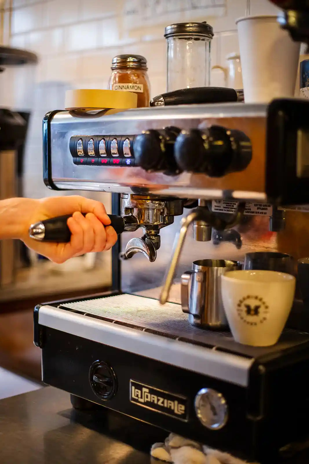 Person operating a La Marzocco espresso machine with a cup on a counter.