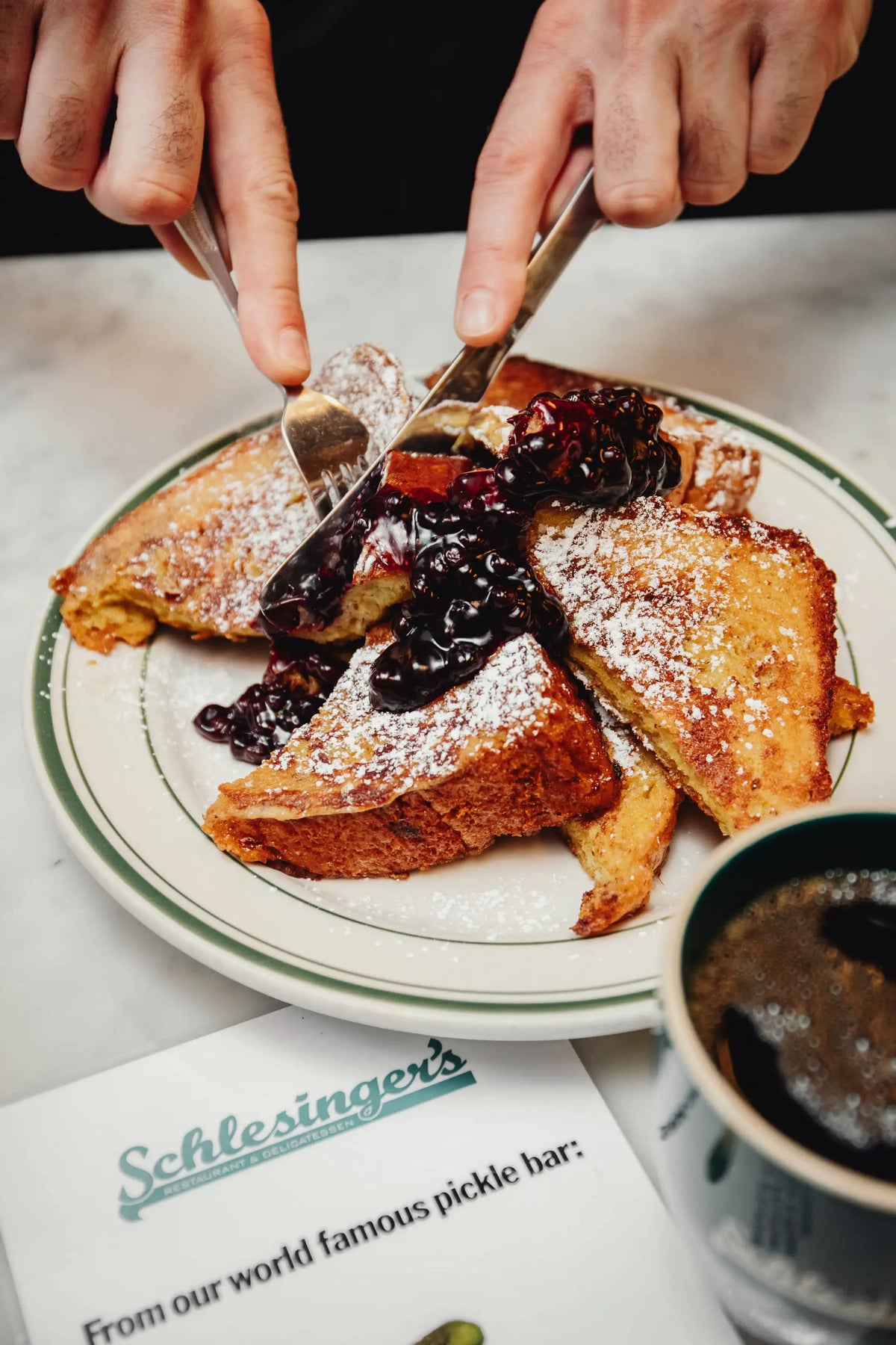 French toast with jam being spread on a plate, with a cup of coffee and a menu in the background.