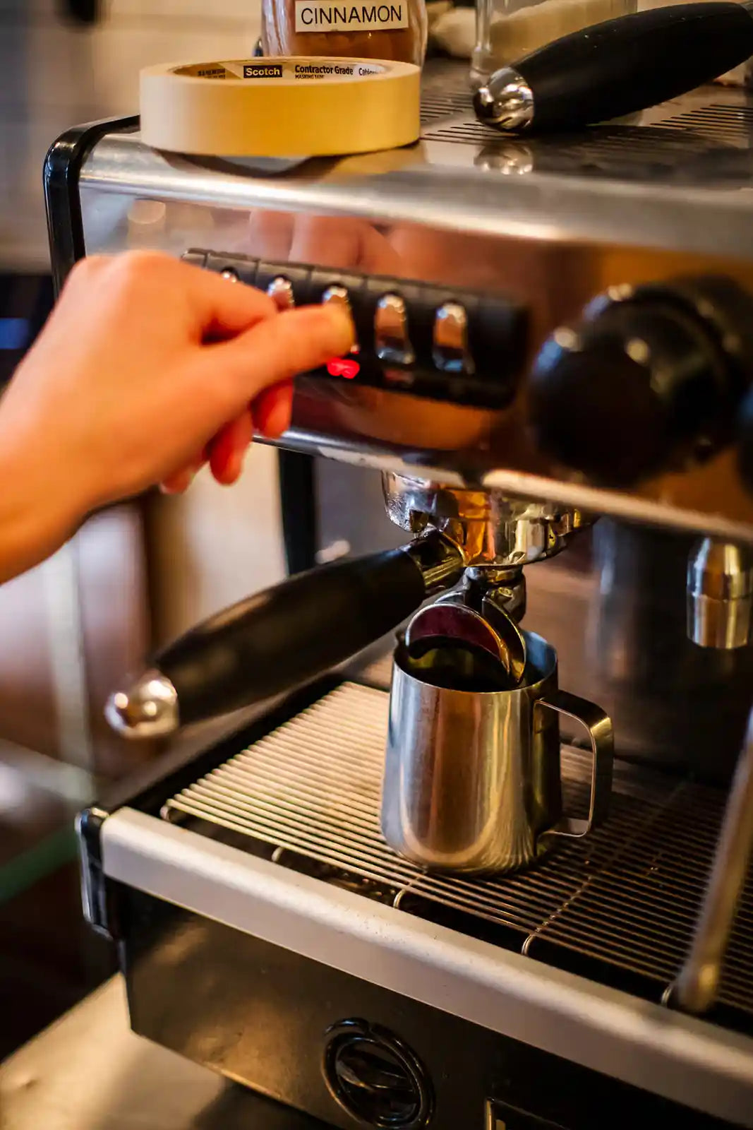 Hand operating an espresso machine with a small container on top