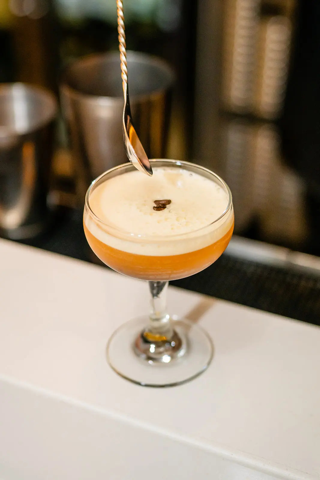 Espresso Martini Cocktail with a layer of foam and a skewer in a glass on a bar counter.