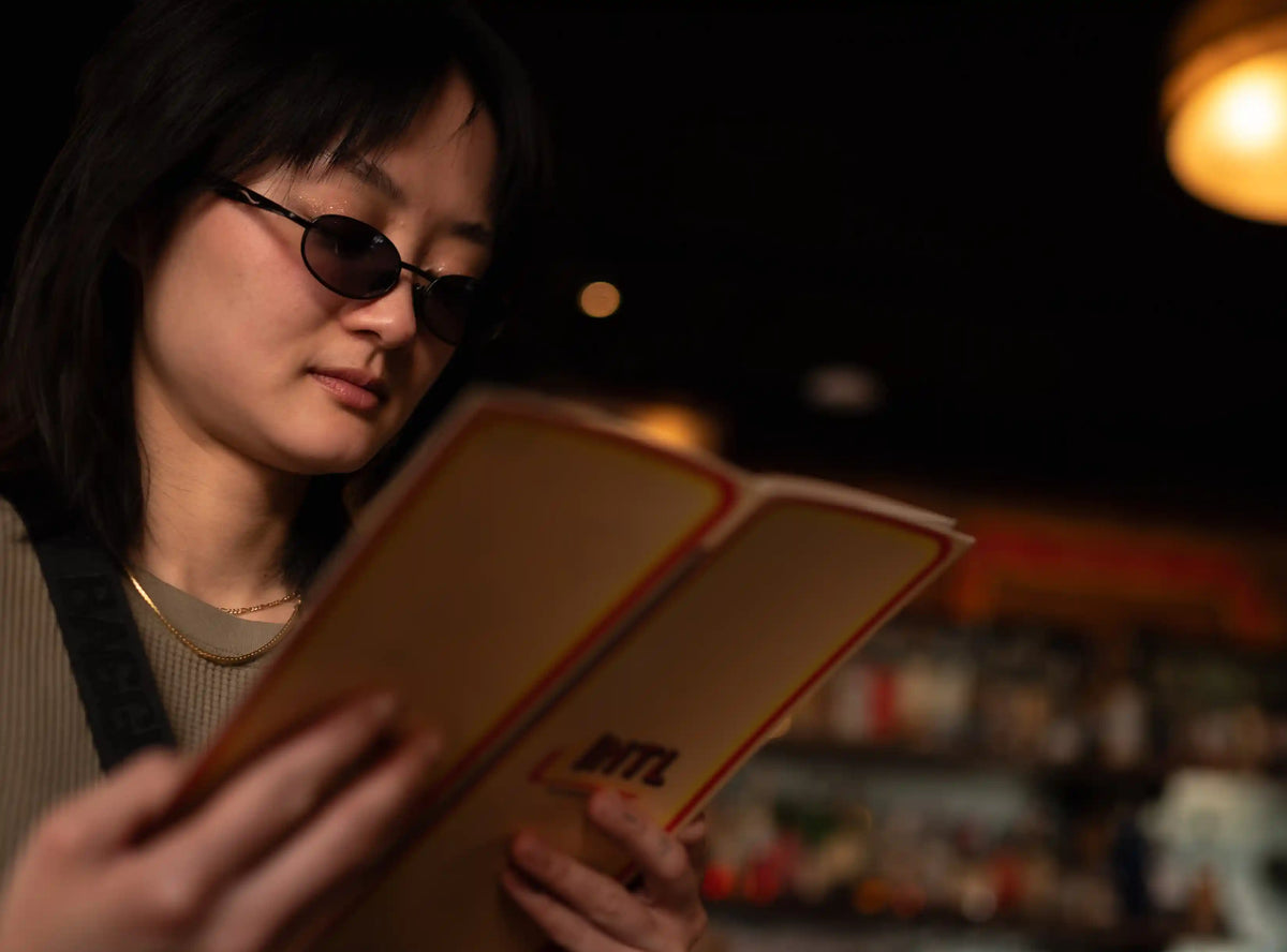 Woman with small black sunglasses reading a menu for The International Bar in Philadelphia, PA