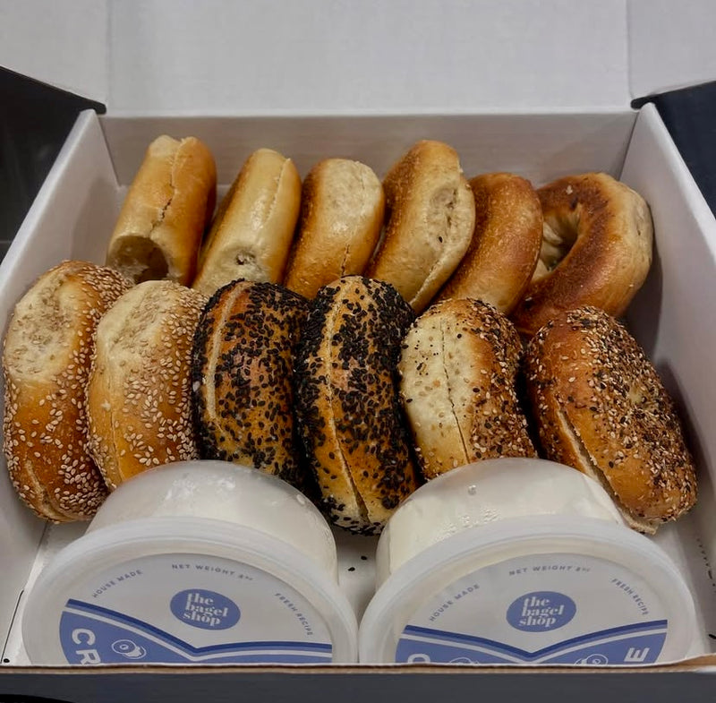 Assorted bagels with different toppings in a box with cream cheese containers.