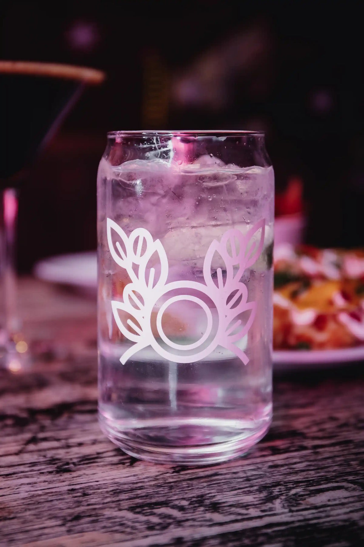 Clear glass with Bean2Bean Coffee Co. Logo on a wooden table with blurred background